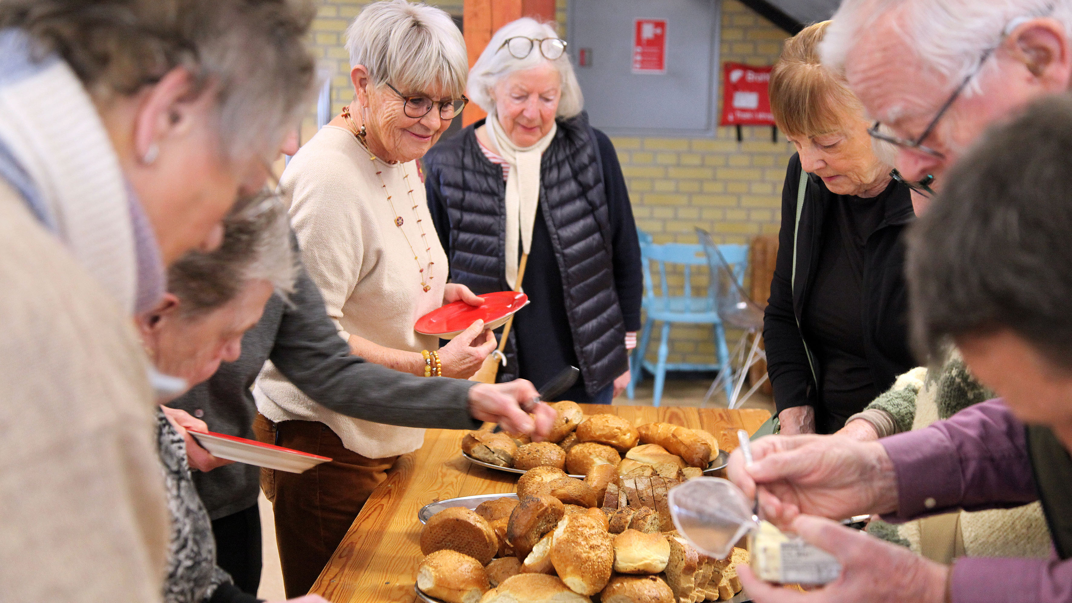 Medlemmer står omkring et langbord med boller og kaffe til fredagsbrød